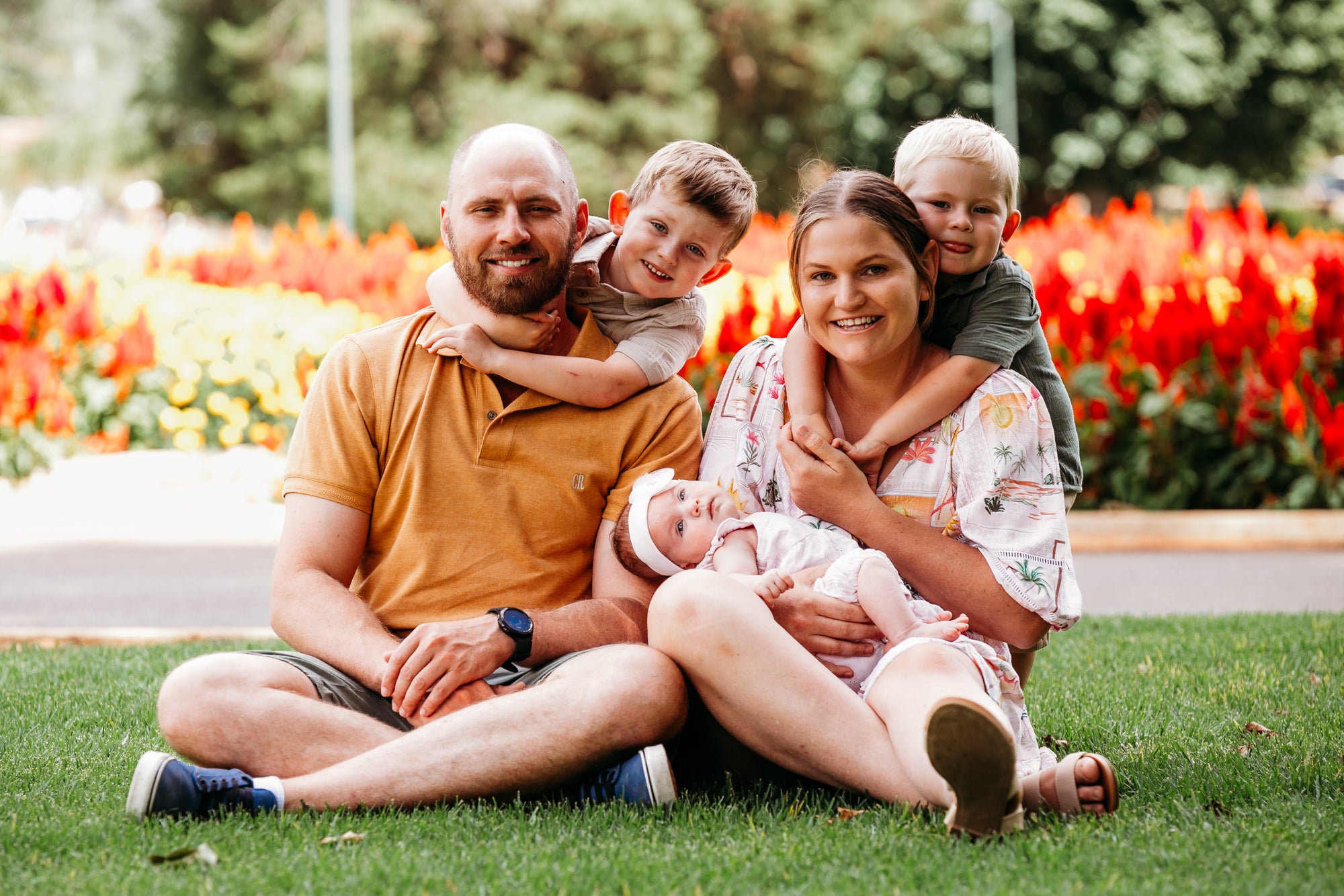 Family of four sitting on grass with flowers in the background